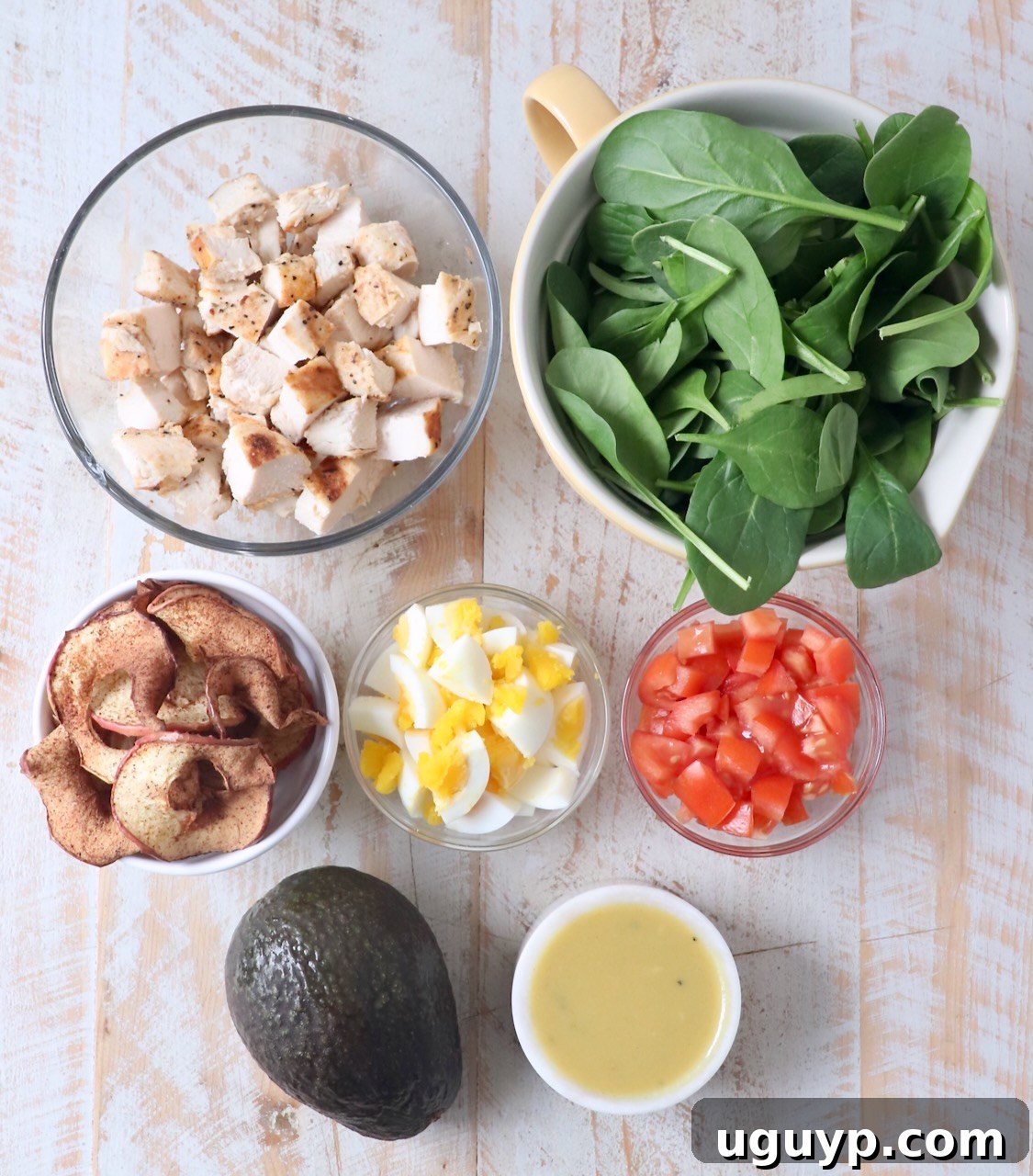 A top-down view of all the fresh ingredients needed for a healthy Cobb Salad, including vibrant spinach, diced tomatoes, grilled chicken breast, perfectly peeled hard-boiled eggs, creamy avocado slices, and crisp apple chips, showcasing the salad's wholesome components.