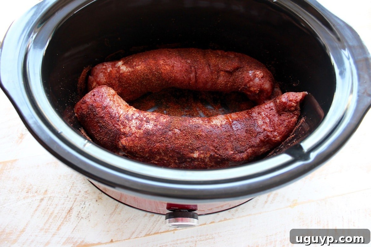 Pork tenderloin seasoned with a spice rub placed in a slow cooker, ready for the honey-lime marinade.