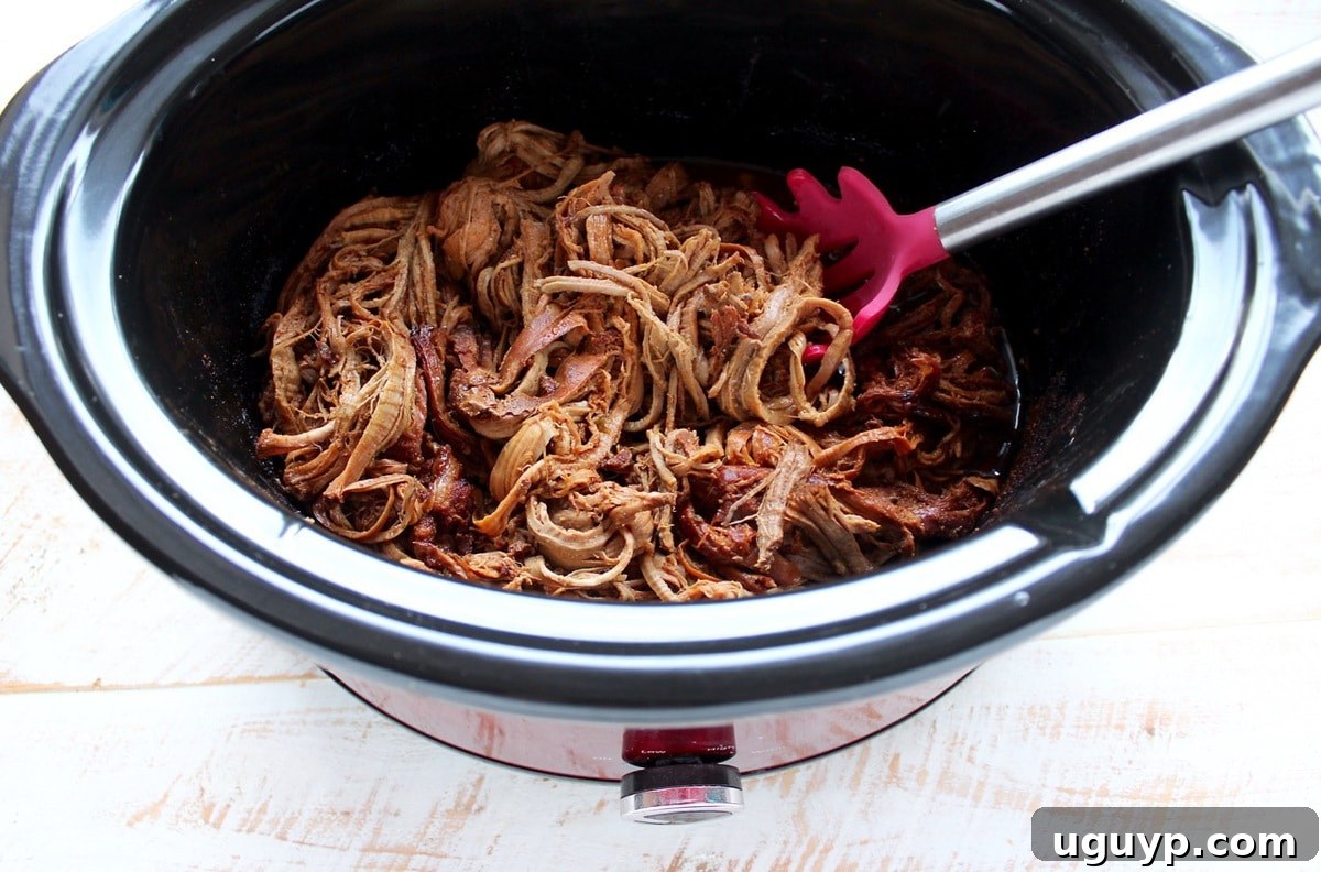 Shredded pulled pork tenderloin with chipotle honey sauce directly in the slow cooker, showing its tender texture.