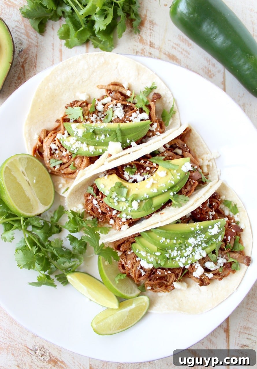 A hand squeezing a lime wedge over a fully assembled Slow Cooker Pulled Pork Tenderloin Chipotle Honey Taco.