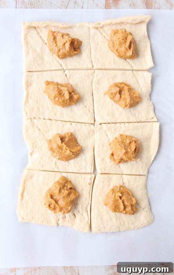 A spoonful of creamy pumpkin and cream cheese filling dolloped onto crescent roll dough squares.