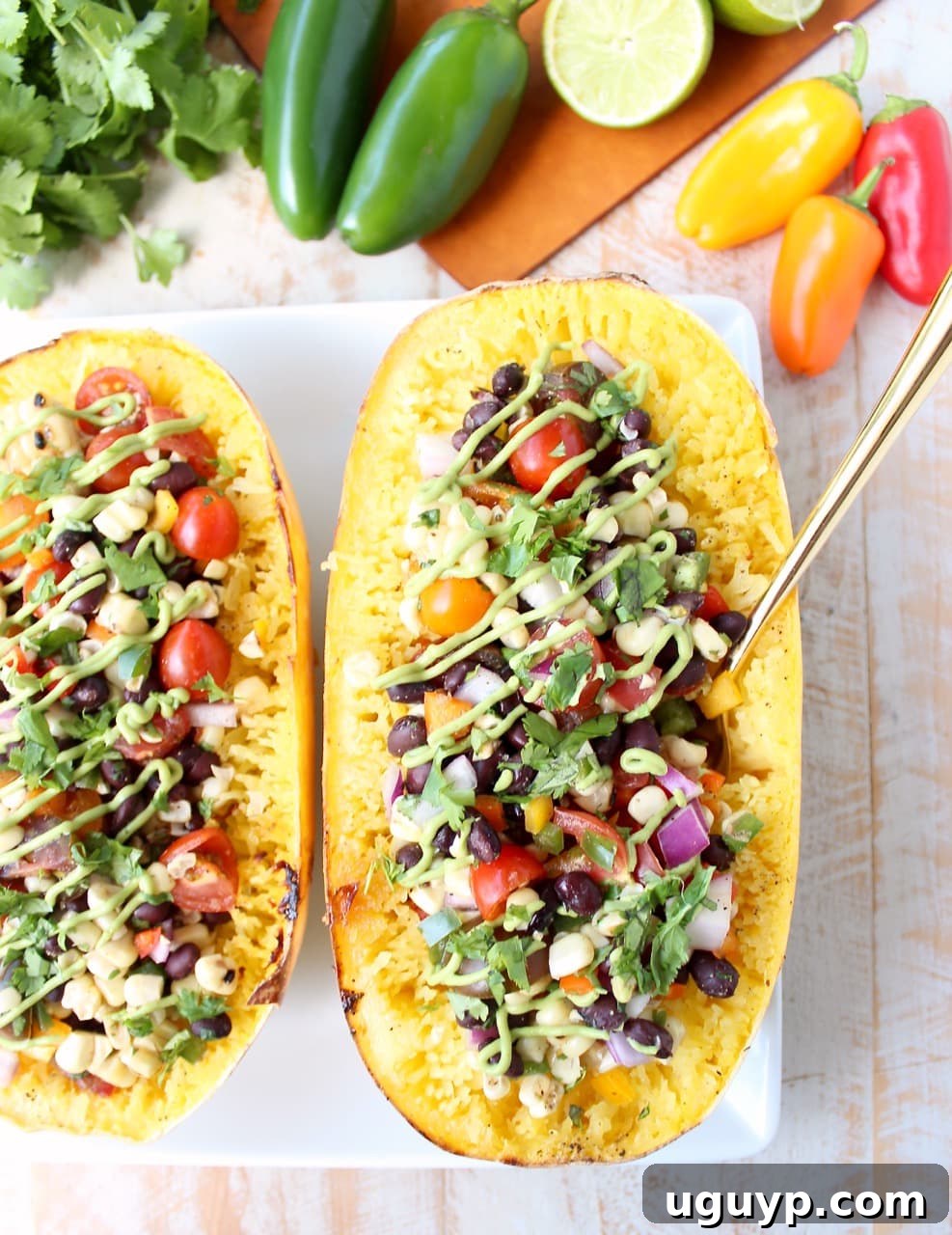 Roasted spaghetti squash halves filled with black bean corn salsa, garnished with avocado dressing on a plate with a fork.