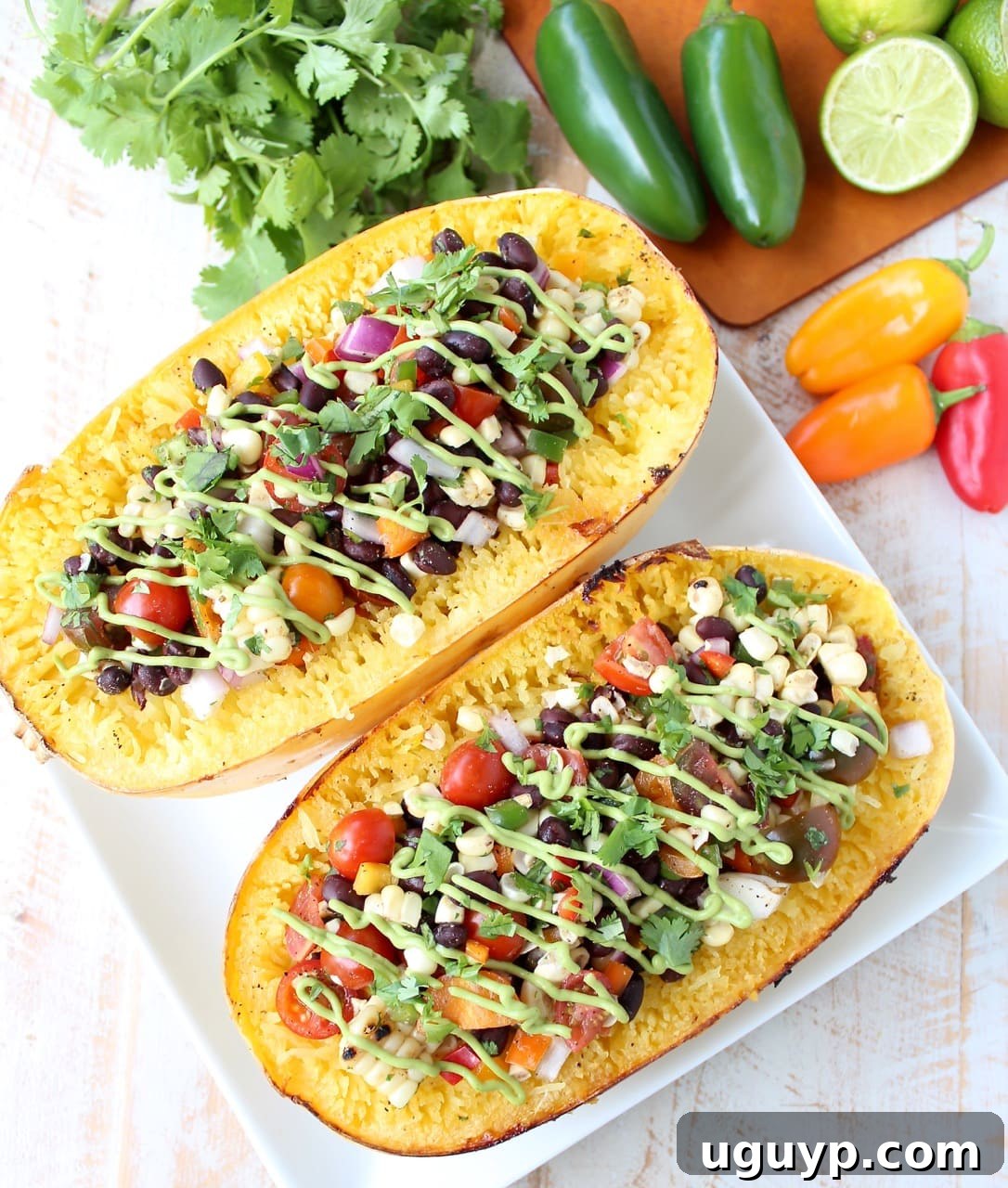 Roasted spaghetti squash filled with colorful black bean corn relish and creamy avocado sauce on a white plate.