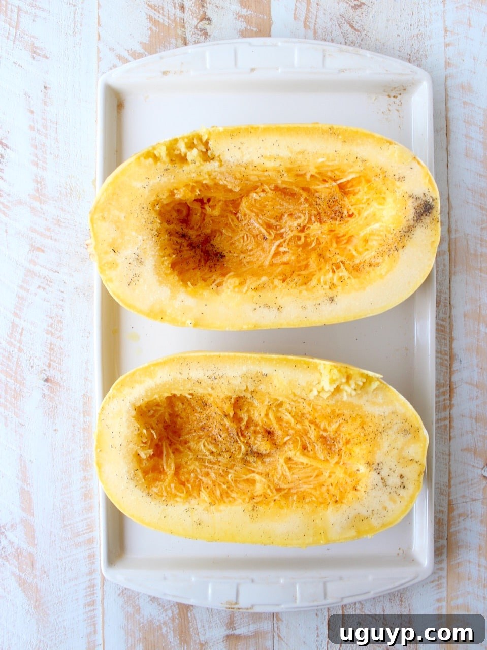 Spaghetti squash sliced in half and seasoned on a baking sheet, ready for roasting.