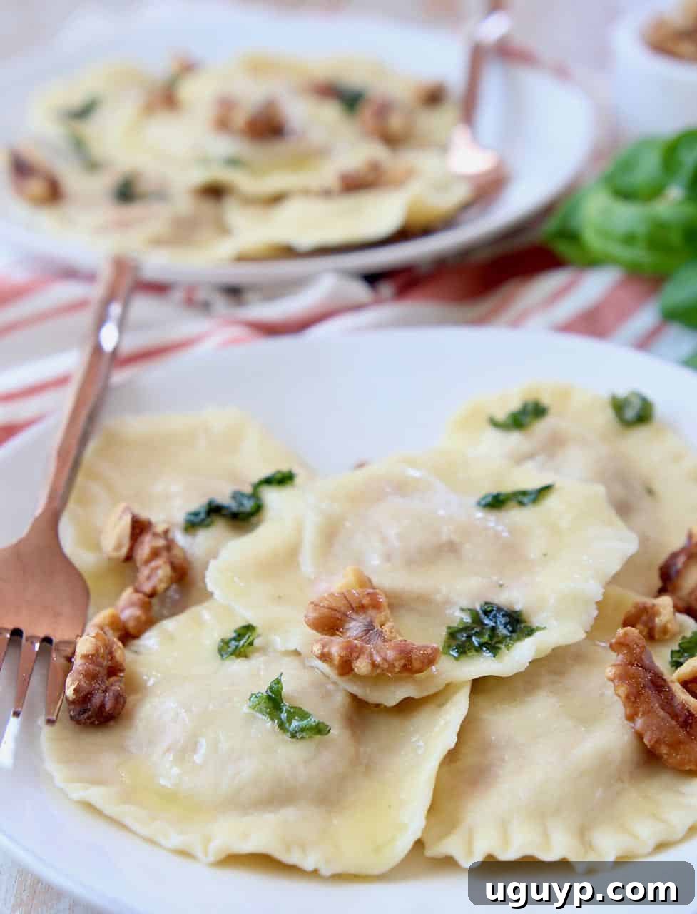 Raviolis on plate topped with basil brown butter sauce and toasted walnuts