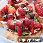 A single piece of strawberry bruschetta, with diced strawberries and fresh basil on toasted bread, presented on a plate.