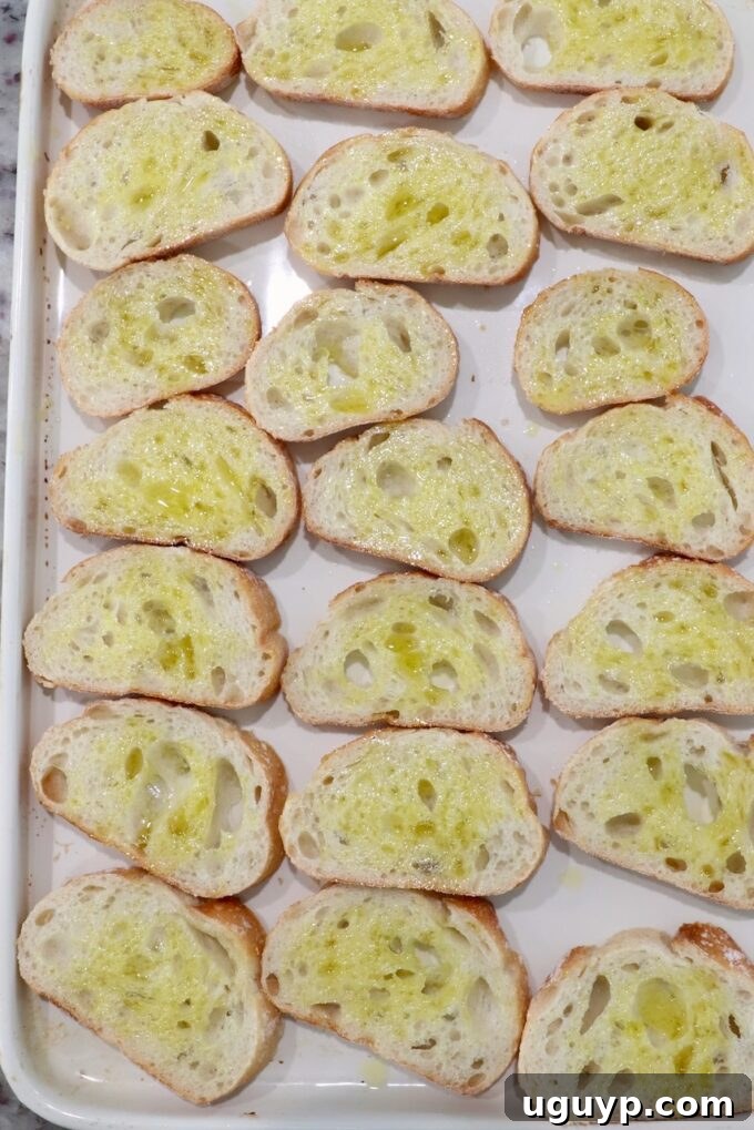 Slices of baguette lightly brushed with olive oil, neatly arranged on a baking sheet, ready for toasting.