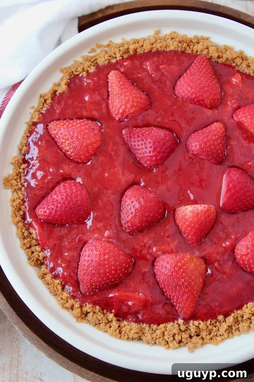 An overhead shot of a vibrant fresh strawberry pie with a graham cracker crust, garnished with whole strawberries.