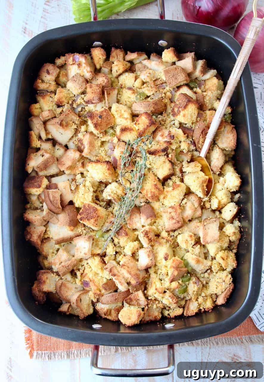 Golden brown gluten-free cornbread stuffing in a roasting pan, garnished with fresh thyme sprigs and a serving spoon.