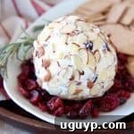 A beautifully garnished Cranberry Goat Cheese Ball, ready to serve, surrounded by fresh rosemary sprigs, scattered dried cranberries, and a selection of crackers on a elegant white plate.