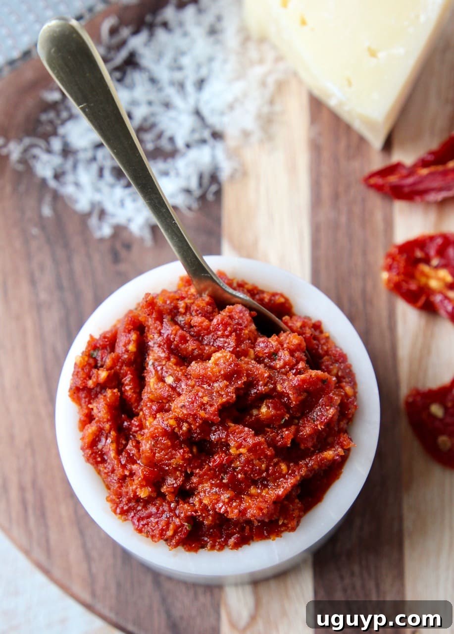 Sun dried tomato pesto in small white bowl with gold spoon in bowl and sun dried tomatoes on the side