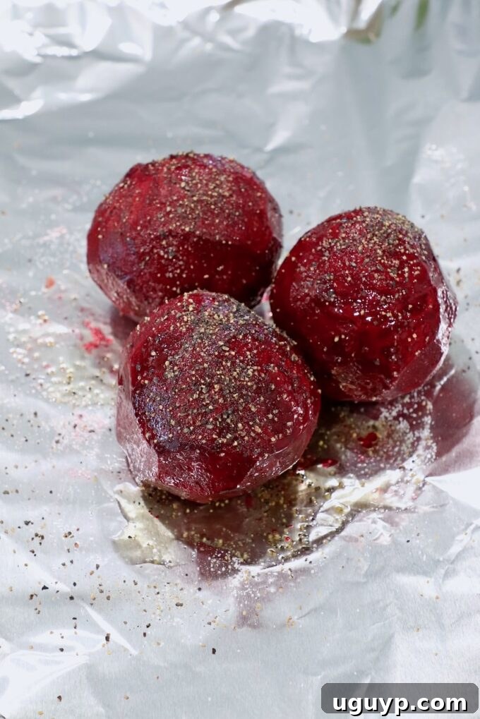 Peeled and seasoned raw beets on a sheet of aluminum foil, ready for roasting.