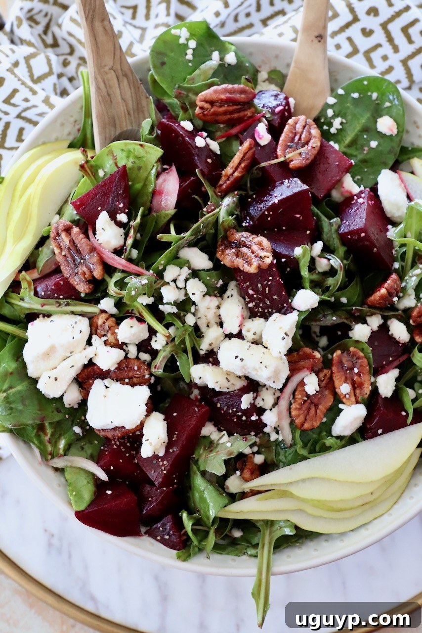A generously sized beet salad in a serving bowl with serving spoons, topped with roasted beets and feta cheese crumbles, ready for sharing.
