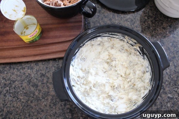 The initial layer of cream cheese and green chilies in a baking dish.