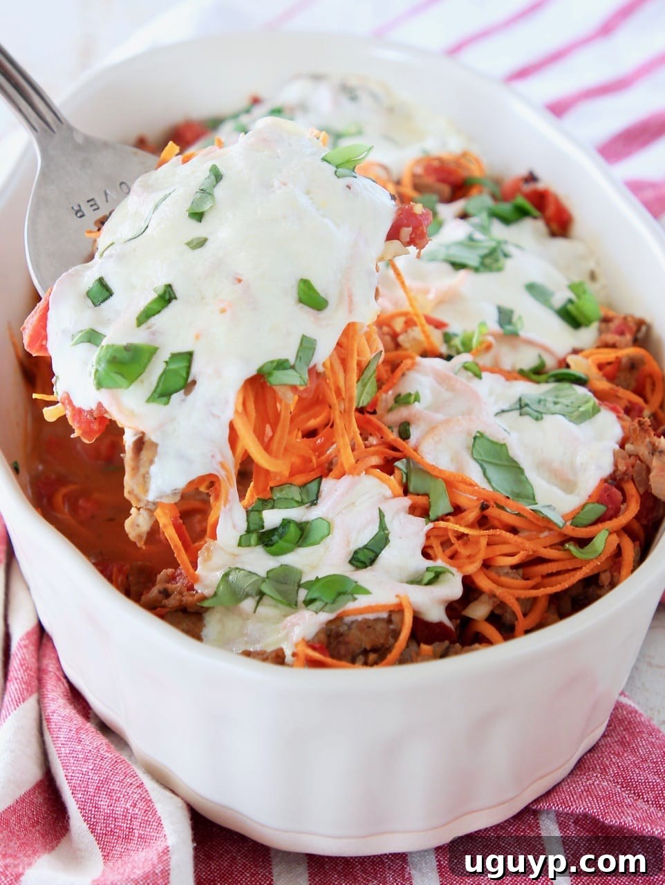 Large fork scooping out of a sweet potato casserole covered in mozzarella cheese