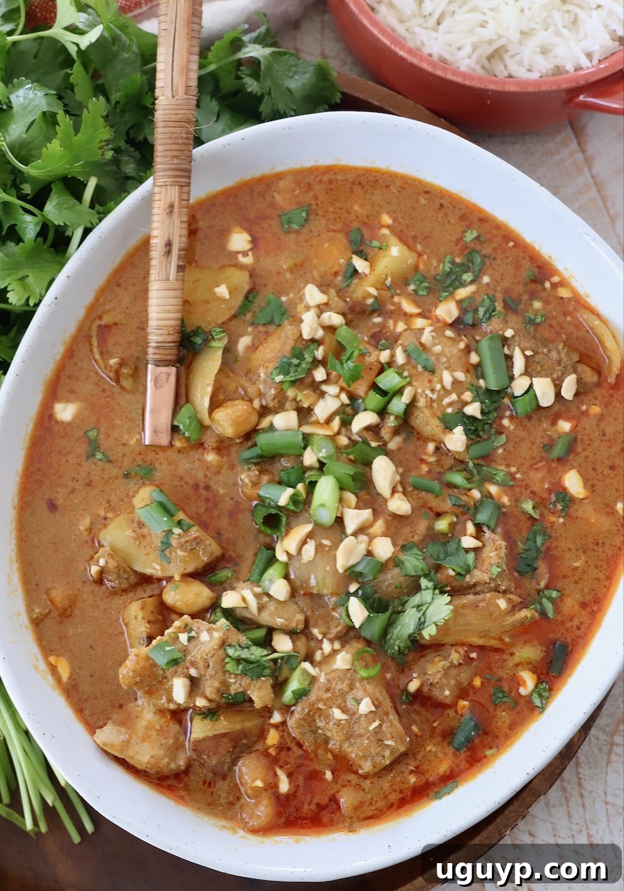A bowl of rich Massaman Curry Chicken with rice, garnished with fresh cilantro and crushed peanuts.