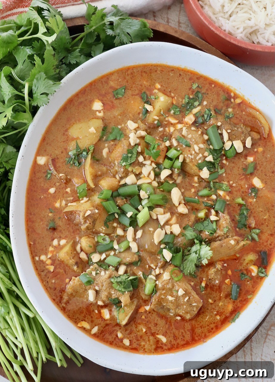 A close-up of Massaman Curry Chicken served in a bowl, garnished with fresh herbs and chopped peanuts.