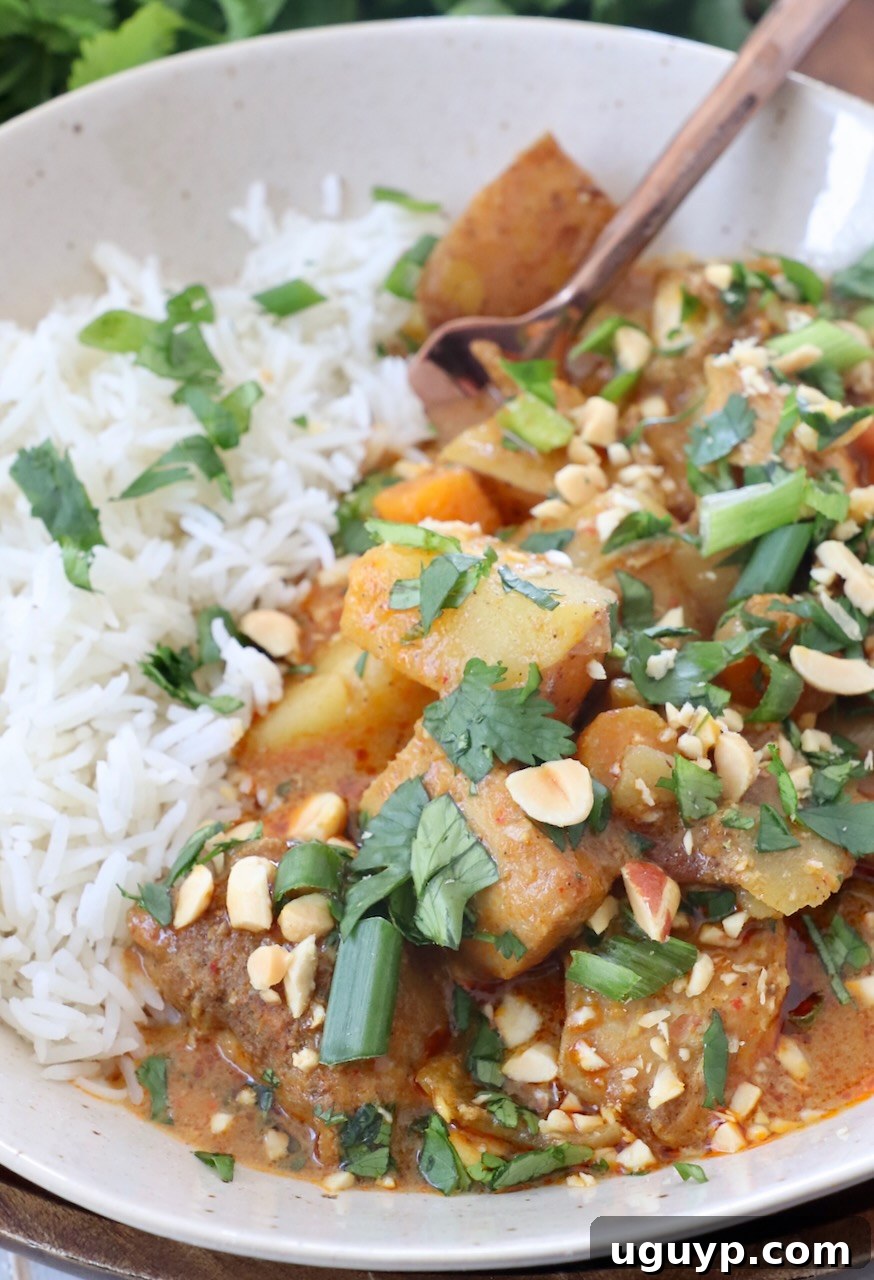 A bowl of Massaman Curry Chicken and vegetables with white rice and a fork, ready to be enjoyed.