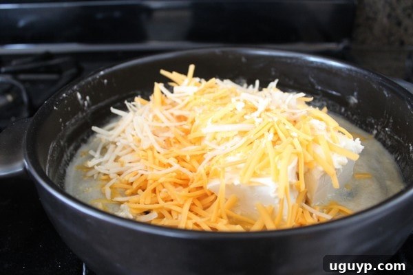 Three different cheeses (cream cheese, cheddar, and parmesan) melting together in a skillet, creating a rich base for the mac and cheese.