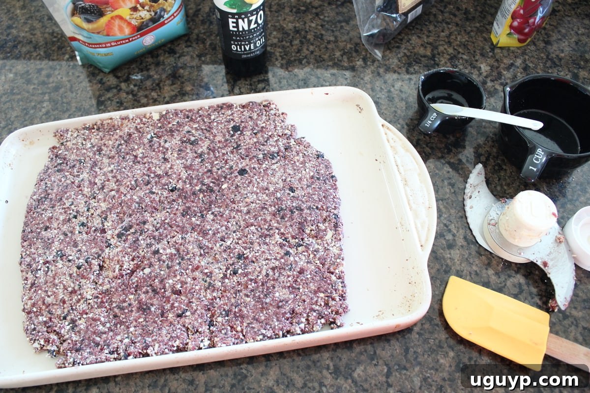 Granola bar mixture being pressed firmly onto a parchment-lined baking sheet.