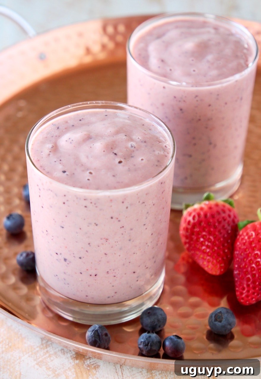Heart healthy fruit smoothie in two glasses on copper tray with fresh strawberries and blueberries