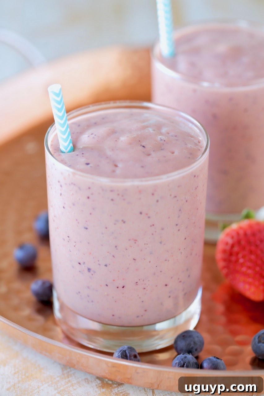 Fruit smoothie in glass with straw on copper tray with fresh strawberries and blueberries