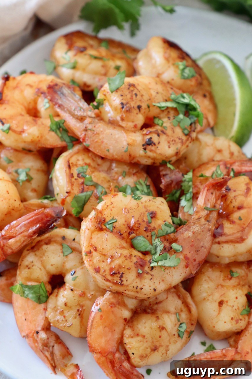 Perfectly grilled shrimp piled on a plate with fresh lime wedges and cilantro