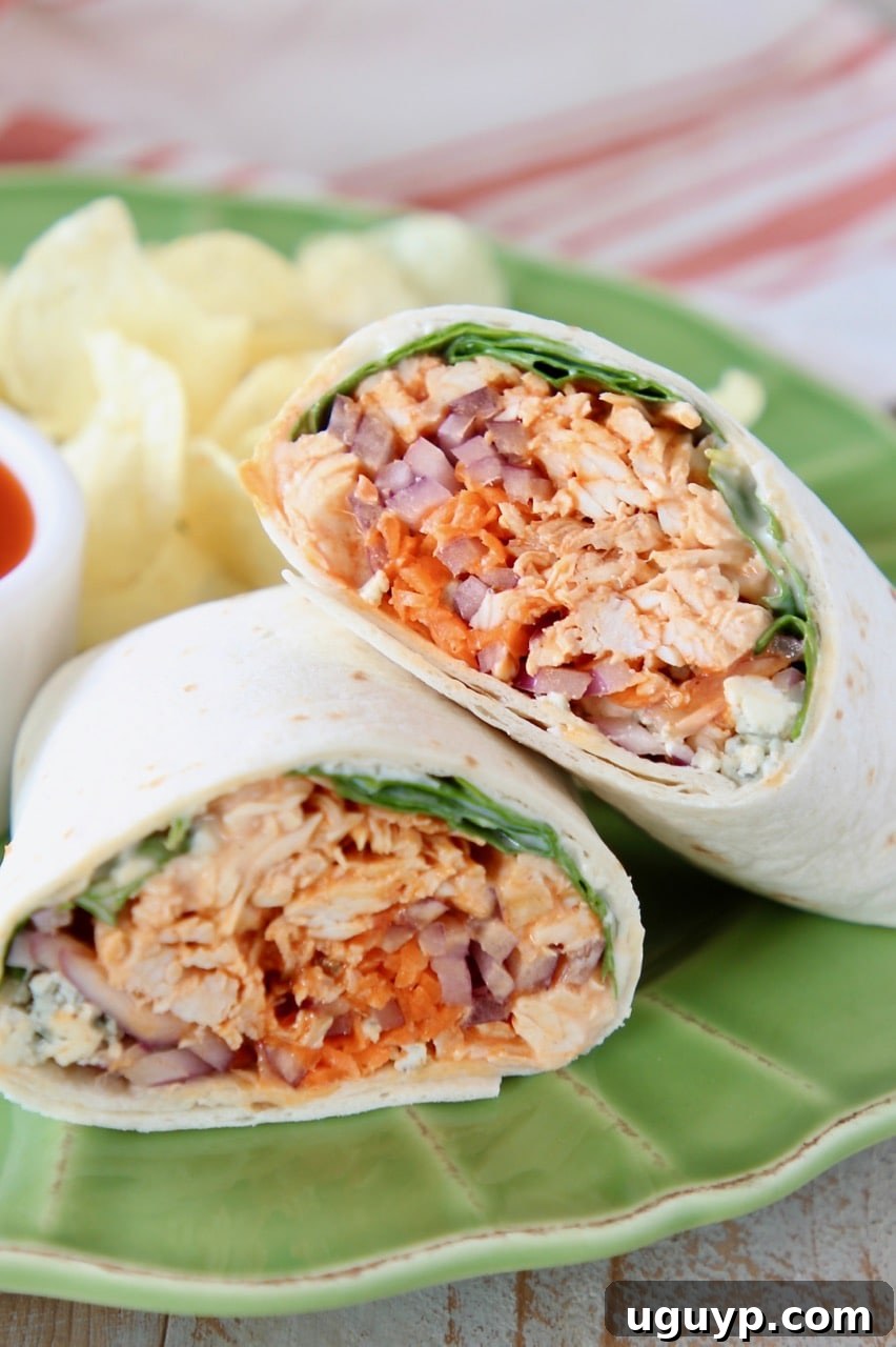 A perfectly cut buffalo chicken wrap, leaning on another half, served on a vibrant green plate with crunchy potato chips, highlighting its deliciousness and ease.