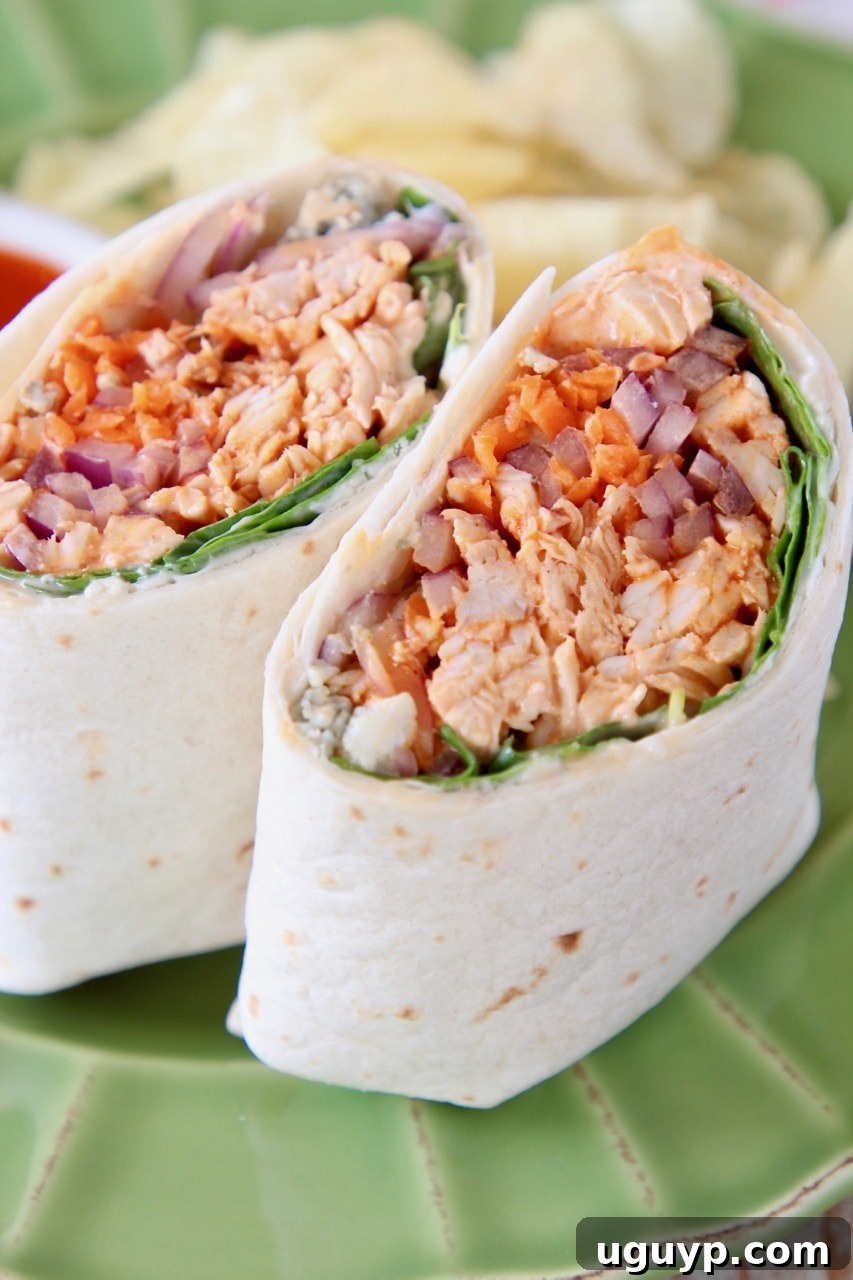 A buffalo chicken wrap, neatly sliced in half, showcasing its rich filling of shredded chicken, vibrant sauce, and fresh greens, presented on a bright green plate.