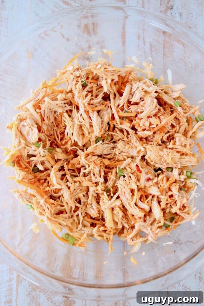 Shredded buffalo chicken filling mixed with vegetables in a glass bowl, ready to be assembled into a crescent ring.