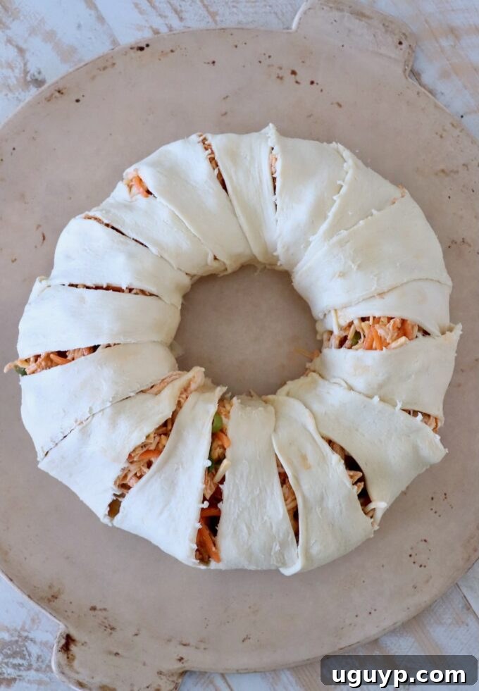 Uncooked buffalo chicken crescent pastry ring arranged on a round stone baking dish, showing the crescent rolls filled and folded.