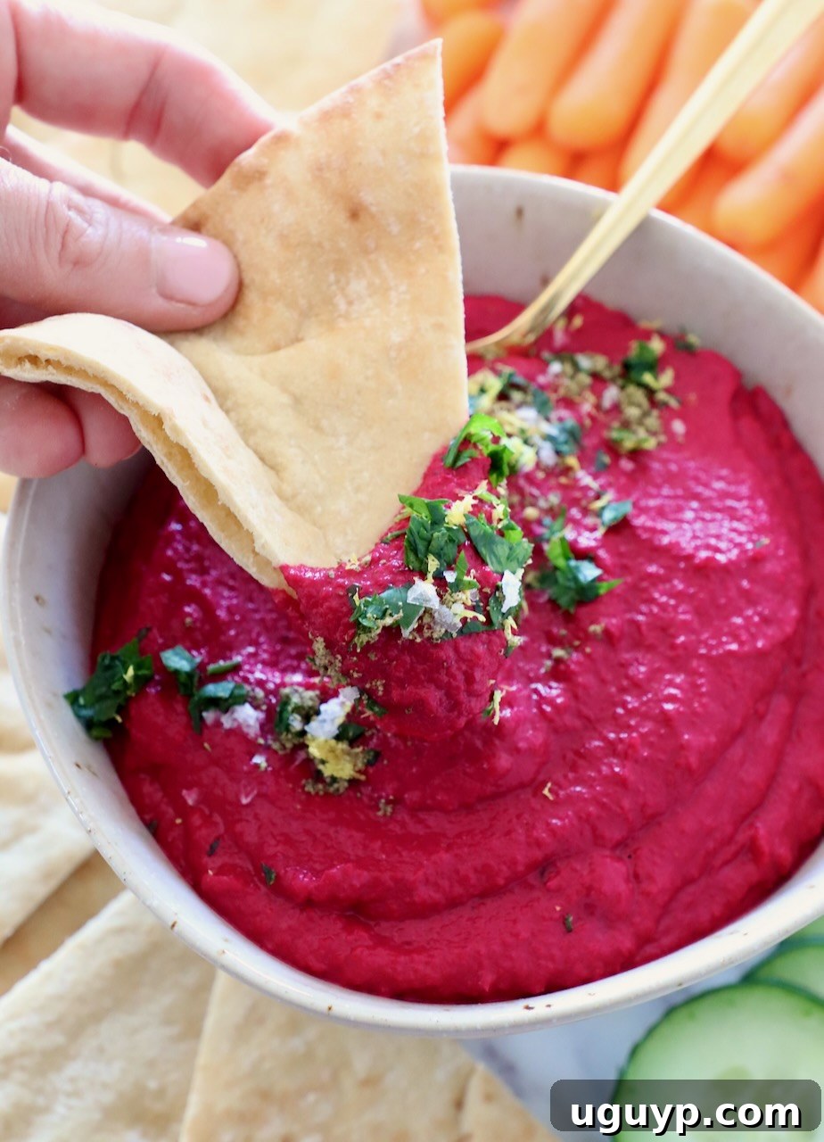 Super creamy beet hummus in a bowl with a piece of pita bread dipped in it, ready to be enjoyed.