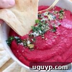 Beet hummus in a bowl with a piece of pita bread dipped into the hummus, ready to be enjoyed.