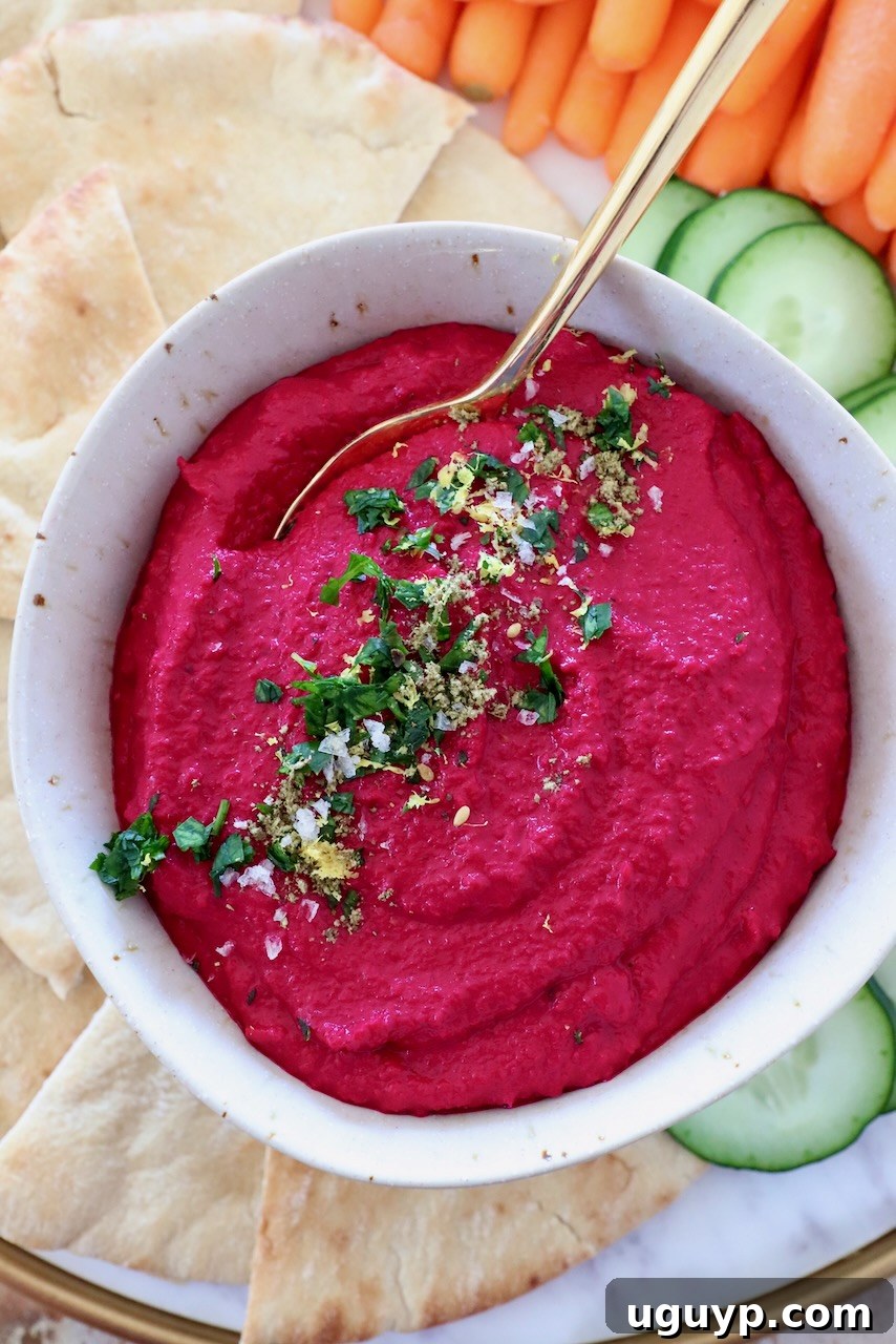 A bowl of vibrant beet hummus with a golden spoon, ready to be served.