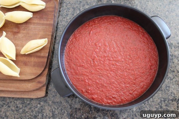 A round baking dish with a base layer of red wine tomato sauce spread evenly.