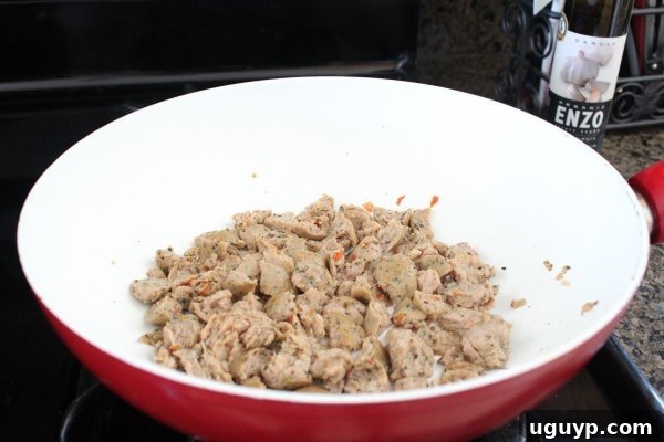 Crumbled sausage cooking in a red and white skillet on the stove.