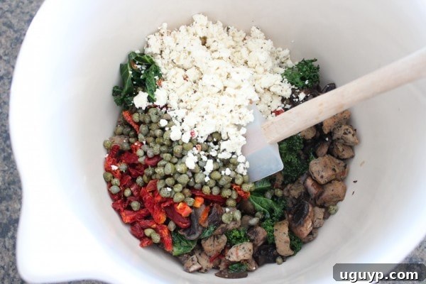 A large white bowl filled with the vibrant sausage, onion, kale, capers, sun-dried tomatoes, and feta cheese filling.