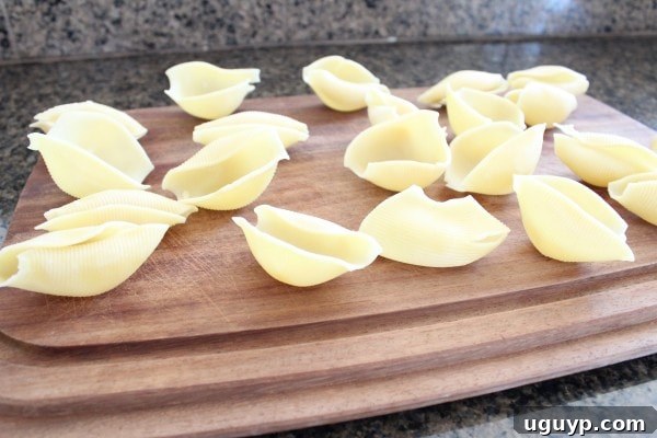 Cooked jumbo pasta shells neatly arranged on a wooden cutting board, ready for stuffing.