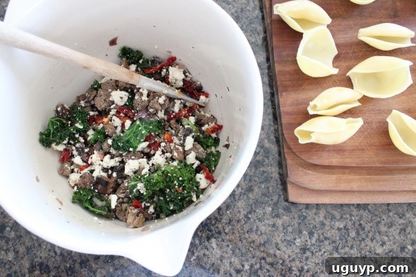 A spoonful of rich sausage filling for stuffed shells being scooped from a large bowl.