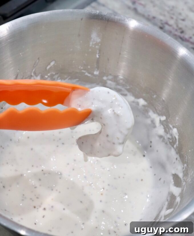 A piece of shrimp being dipped into the prepared batter with tongs, ensuring full coverage.