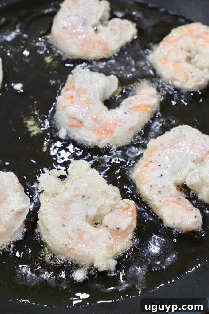 Battered shrimp sizzling and cooking in hot oil in a large skillet.