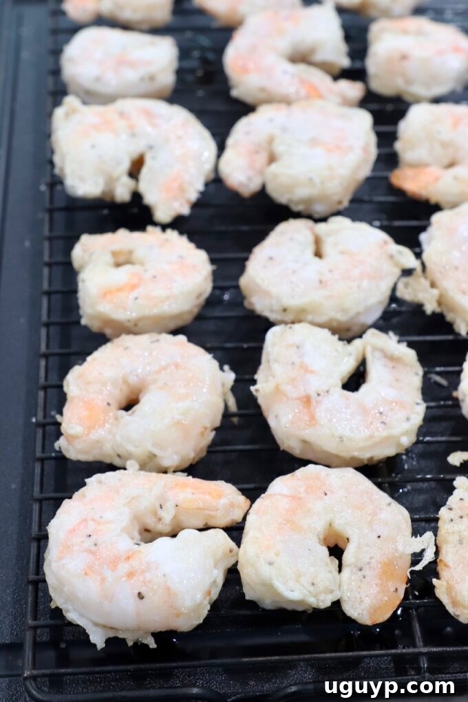 Crispy, battered shrimp resting on a wire rack after frying, allowing excess oil to drain.