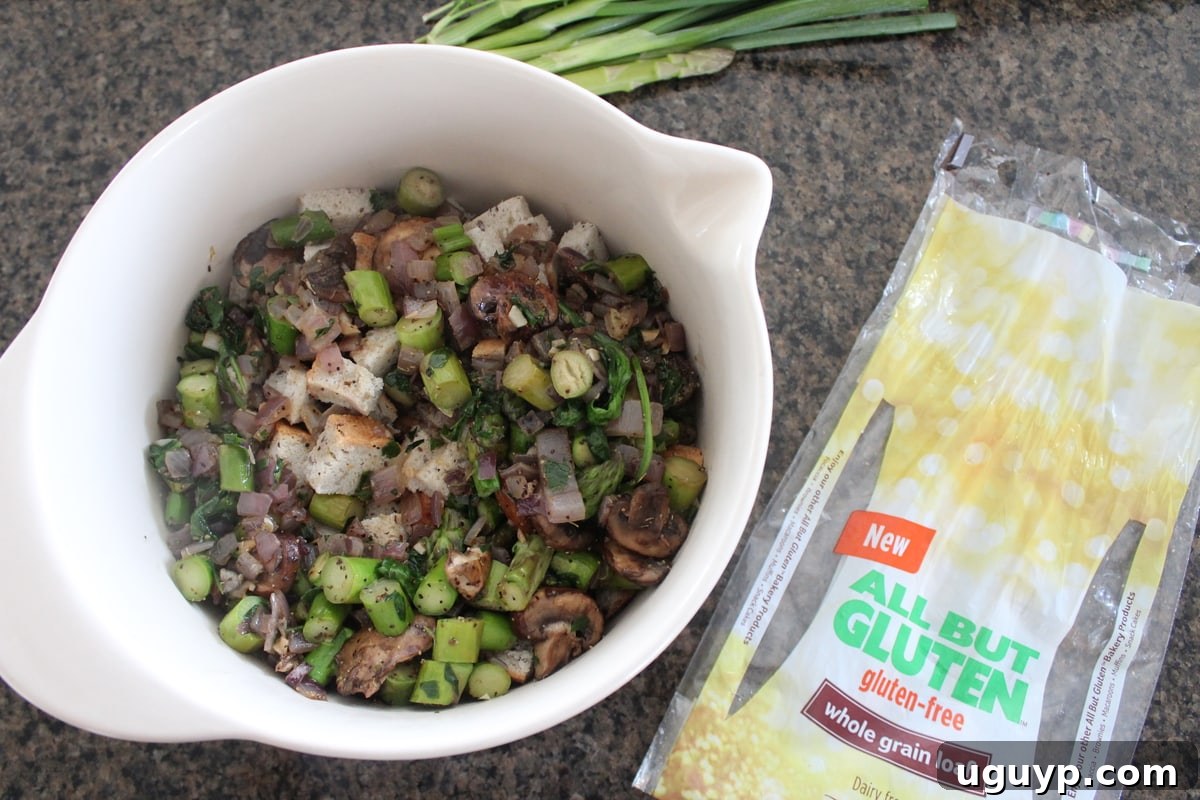 Cooked vegetables and dried gluten-free bread cubes mixed in a large bowl, ready for the liquid ingredients