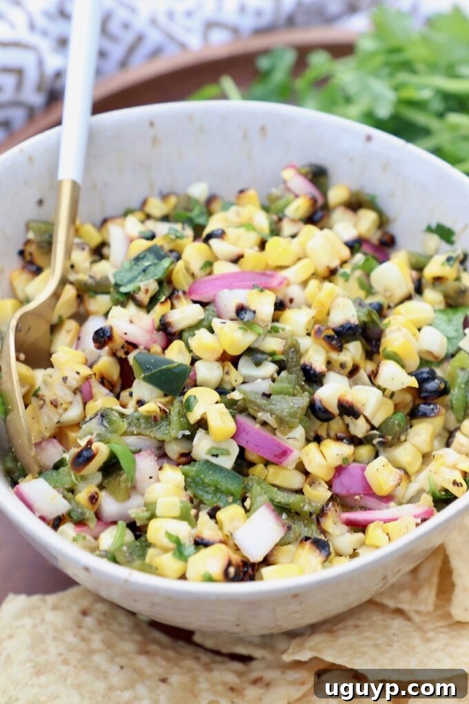 A serving of corn salsa in a white bowl, accompanied by a spoon, highlighting its fresh and vibrant appearance.