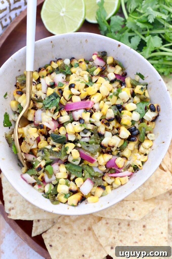 A bowl of vibrant corn and pepper salsa, garnished with fresh herbs and a spoon for serving, showcasing its appealing texture.