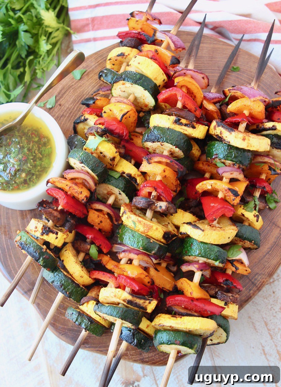 skewers of grilled vegetables on wood serving tray with chimichurri sauce on the side