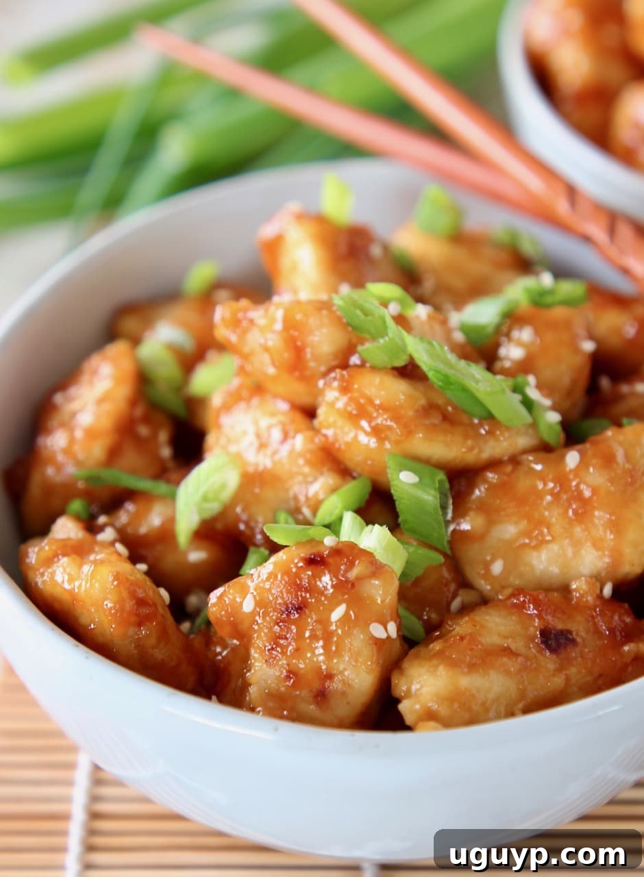 orange chicken in bowl with diced scallions and chopsticks