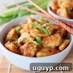 Orange chicken in bowl with scallions and wood chopsticks