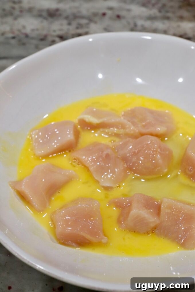 pieces of chicken dipped in a whisked egg in a bowl