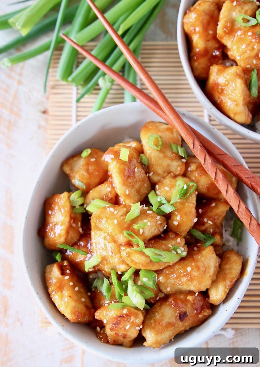 Orange chicken in bowl with diced scallions and wood chopsticks